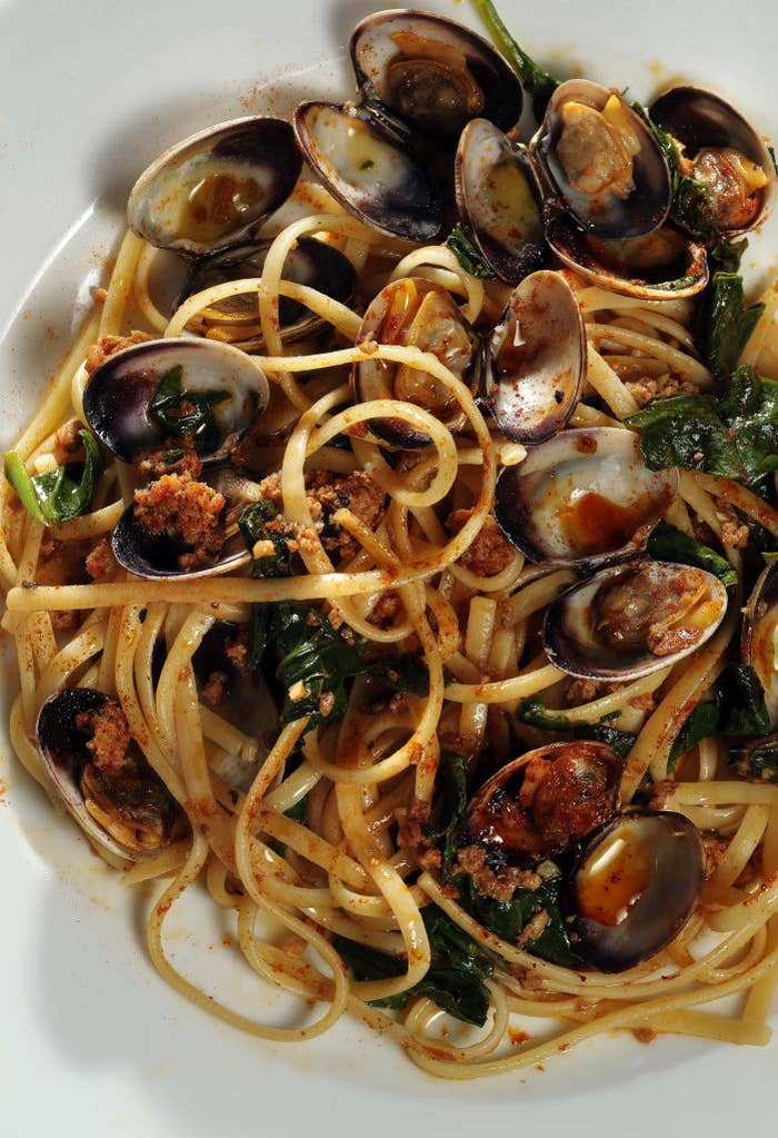 A close-up of a dish featuring linguine pasta with clams, garnished with herbs and what appears to be breadcrumbs