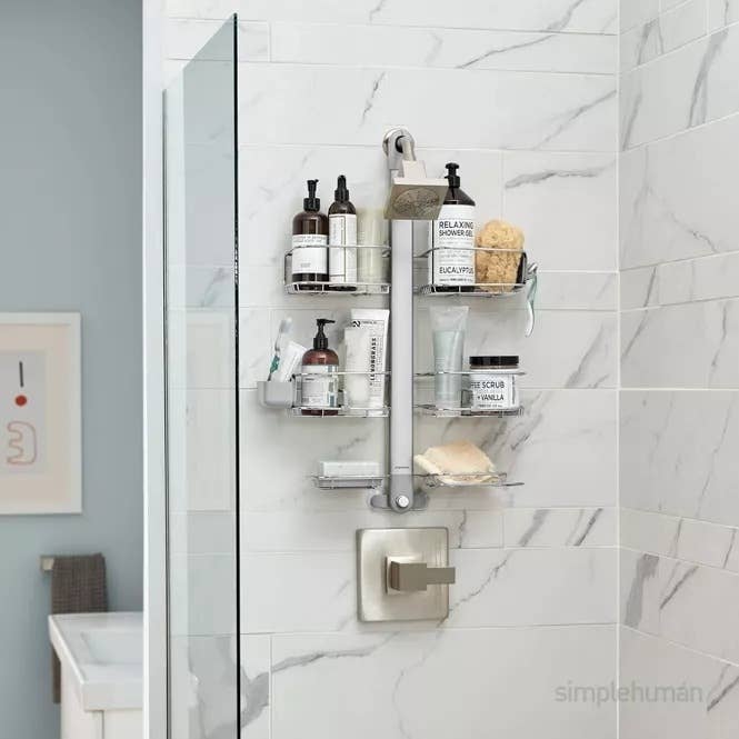 A neatly organized shower caddy holding various bath products, including bottles, soap, a brush, and scrub. The caddy is affixed to a modern, marble-tiled shower wall