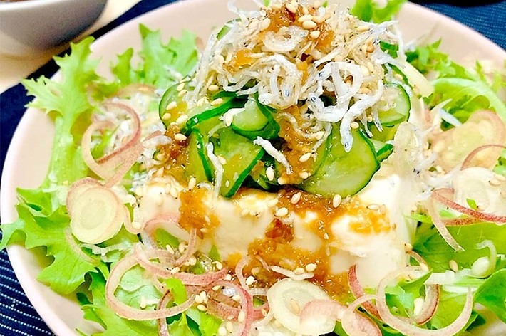 豆腐の上にキュウリ、ネギ、ジャコがトッピングされたサラダ。ドレッシングが添えられています。