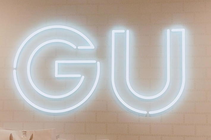 Large illuminated “GU” sign on a wall above white shopping bags. Sign below reads “Gift Wrapping +¥190”