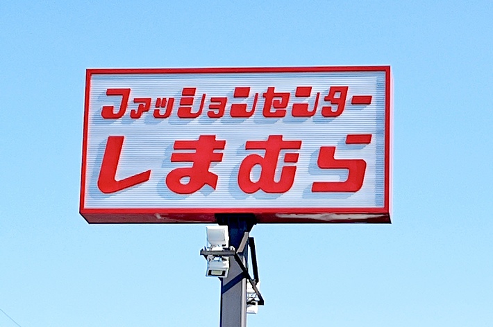 赤地に白文字の「ファッションセンターしまむら」の看板が青空を背景に立っている。