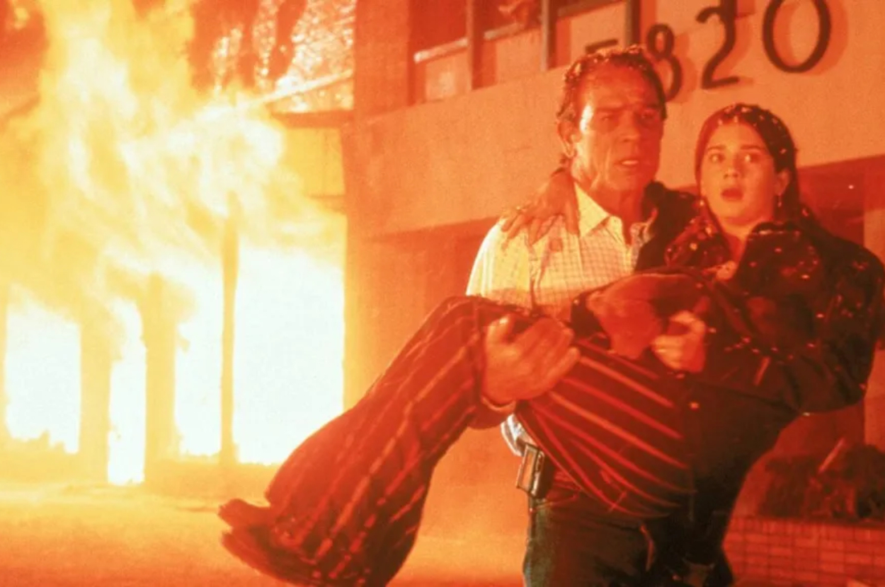 A man is carrying a child away from a burning building marked 820, both appearing tense and determined