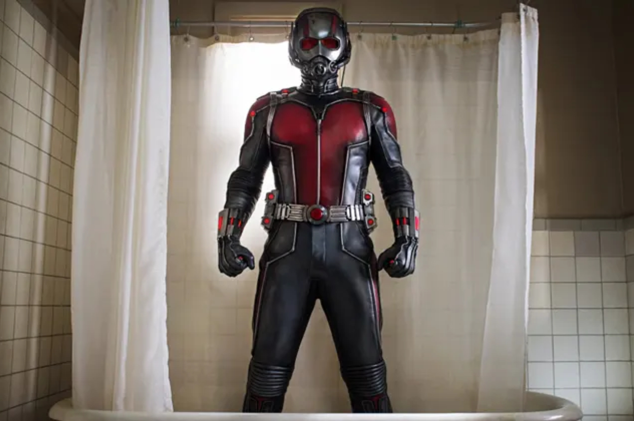 Ant-Man, dressed in his superhero suit, stands confidently in a bathroom with a white shower curtain behind him