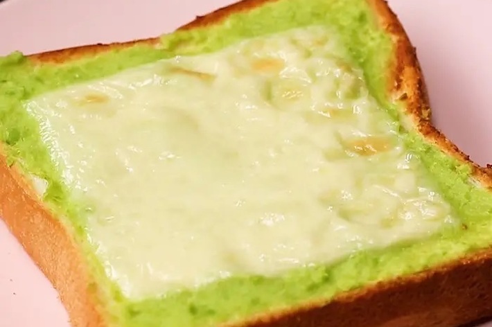 パンの上に緑色のペーストとチーズがのっているトースト。