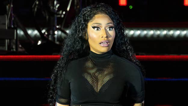 Nicki Minaj performs on stage, wearing a black mesh top with long, wavy hair and dramatic makeup, looking surprised