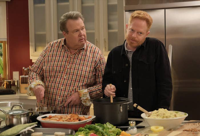 Eric Stonestreet and Jesse Tyler Ferguson are in a kitchen cooking. Eric holds a pan while Jesse stirs a pot. Various ingredients are on the counter