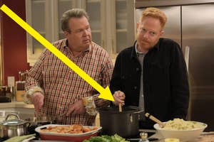 Eric Stonestreet, in a plaid shirt, and Jesse Tyler Ferguson, in a dark jacket, are in a kitchen. Jesse stirs a pot while Eric looks at him. Arrow pointing at pot