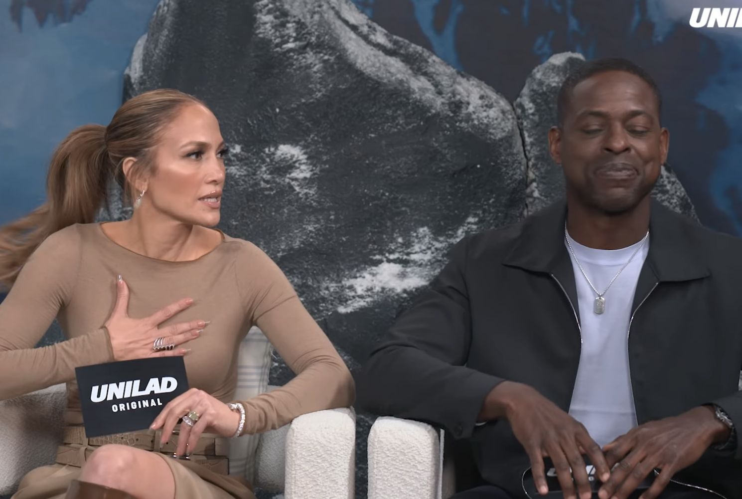 Jennifer Lopez, Simu Liu, and Sterling K. Brown are seated, discussing A.I. related fears in a YouTube video by Unilad