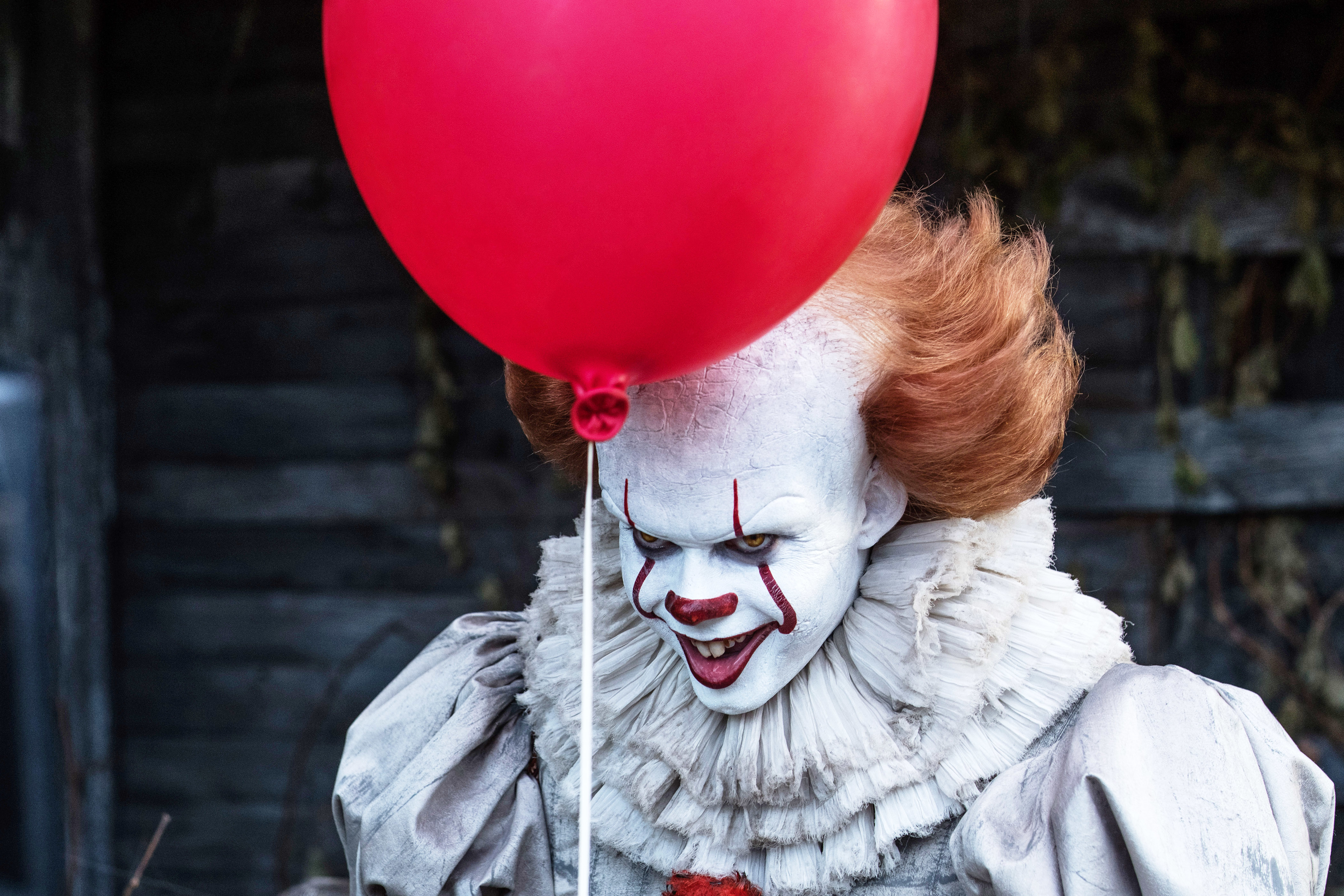 Pennywise, from the movie &quot;IT,&quot; grinning menacingly while holding a red balloon