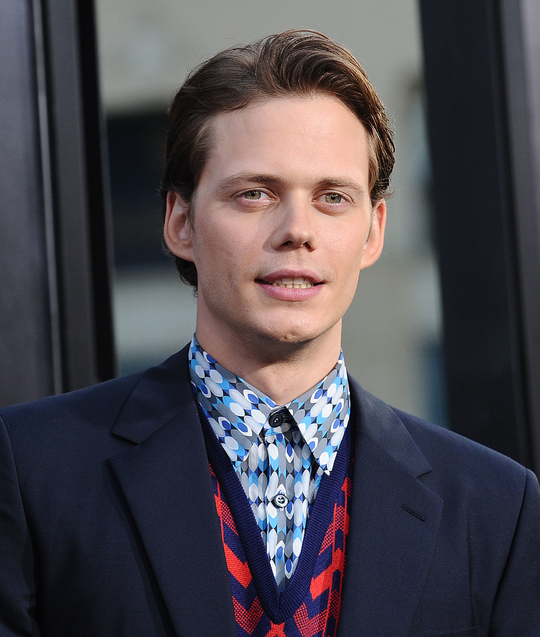 Bill Skarsgard wears a patterned shirt, a tie, and a blazer. They are at an event