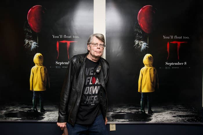 Stephen King stands in front of two &quot;IT&quot; movie posters featuring a child in a yellow raincoat holding a red balloon