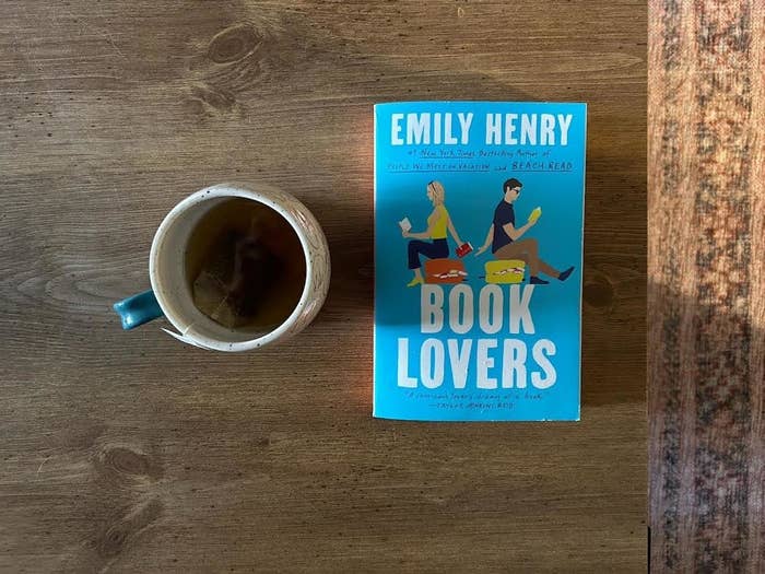 Book "Book Lovers" by Emily Henry on a wooden table next to a mug of tea