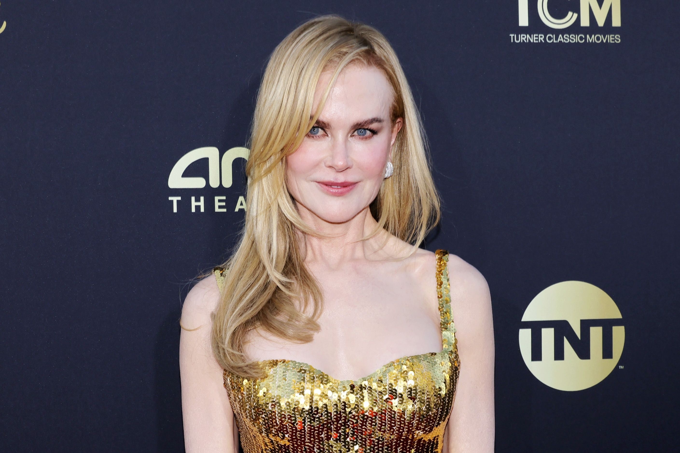 Nicole Kidman at an event, wearing a sparkly, fitted dress with a glittering pattern. The background has logos for Turner Classic Movies and TNT