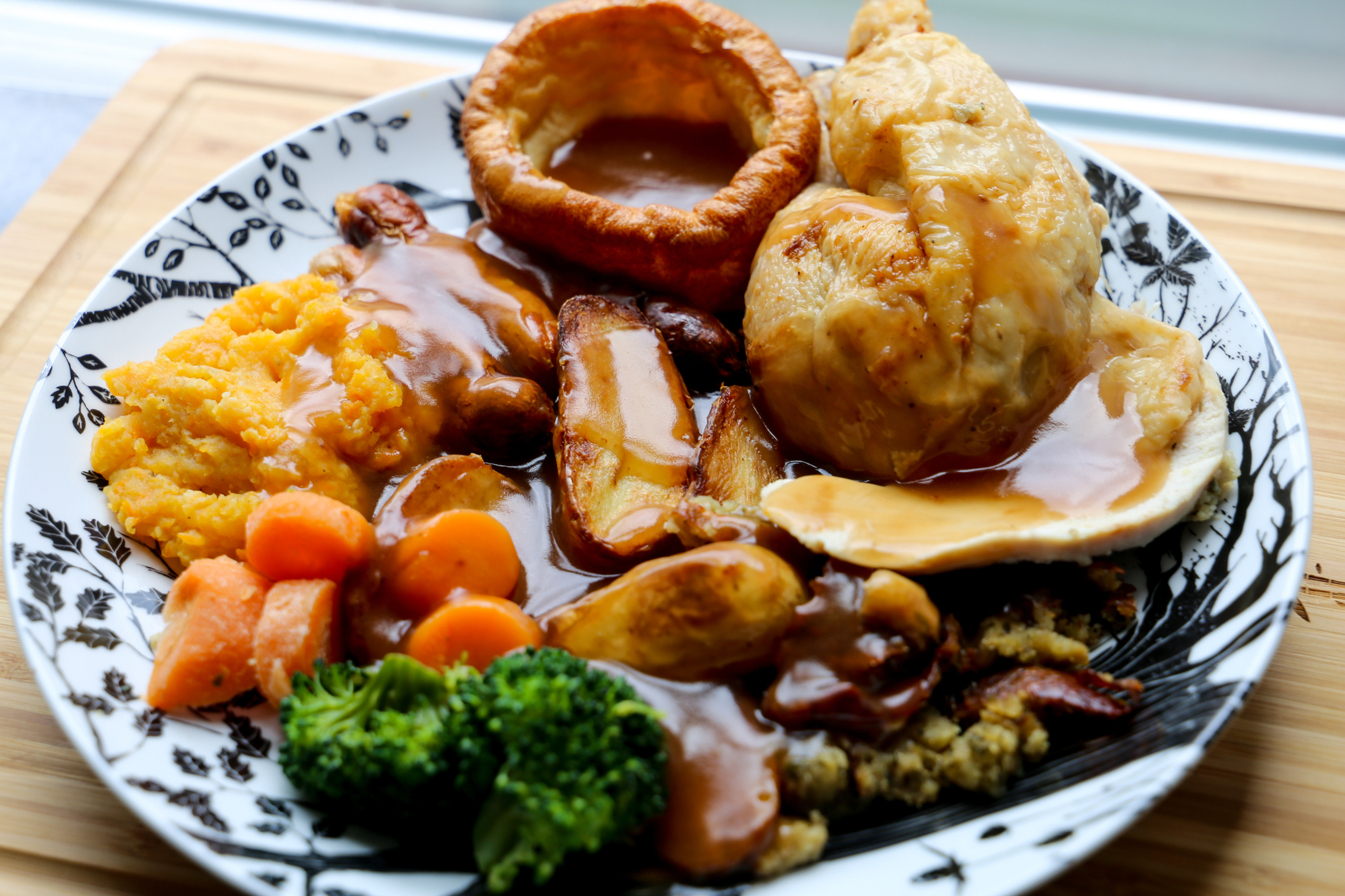 A plate of food with roast chicken, gravy, mashed potatoes, Yorkshire pudding, carrots, broccoli, and roasted potatoes