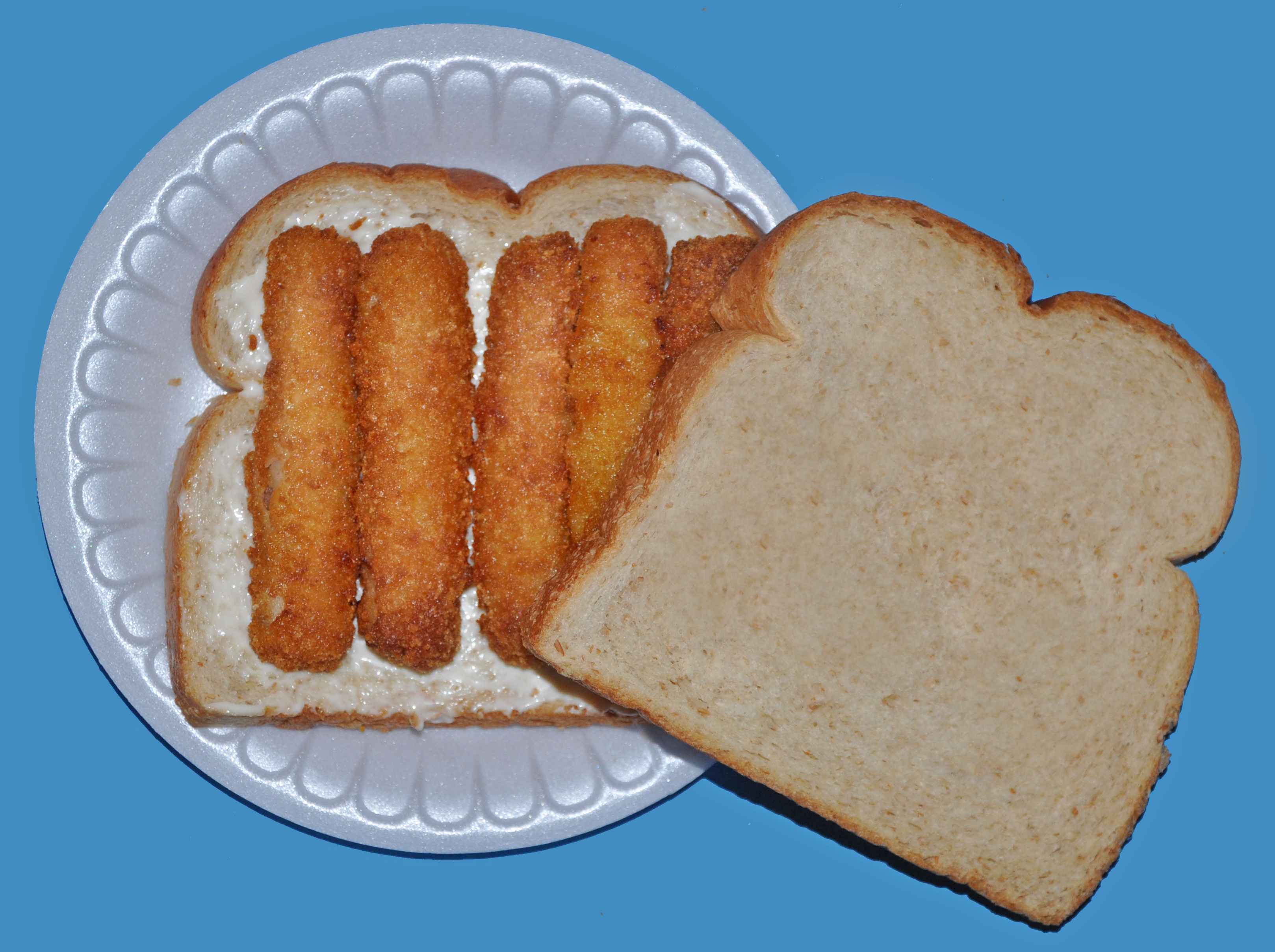 Two slices of bread with fish sticks and tartar sauce on a foam plate