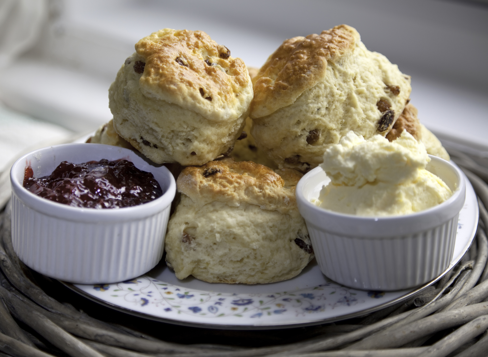 A plate of scones with raisins, accompanied by small bowls of strawberry jam and clotted cream