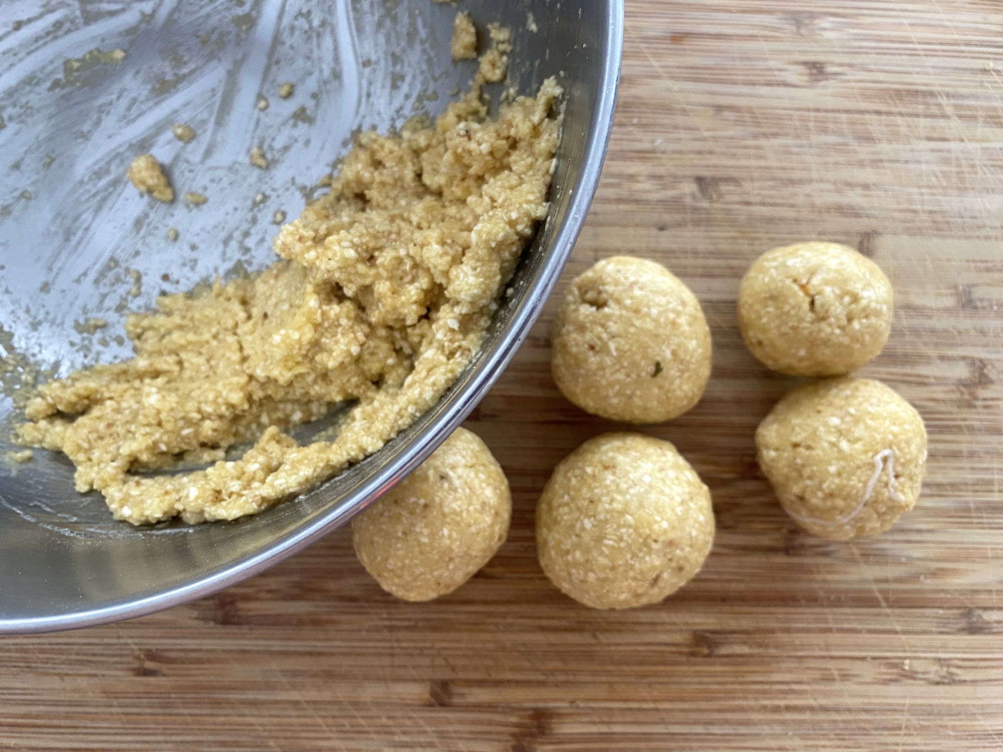 A mixing bowl with cookie dough and five rolled cookie dough balls on a wooden cutting board