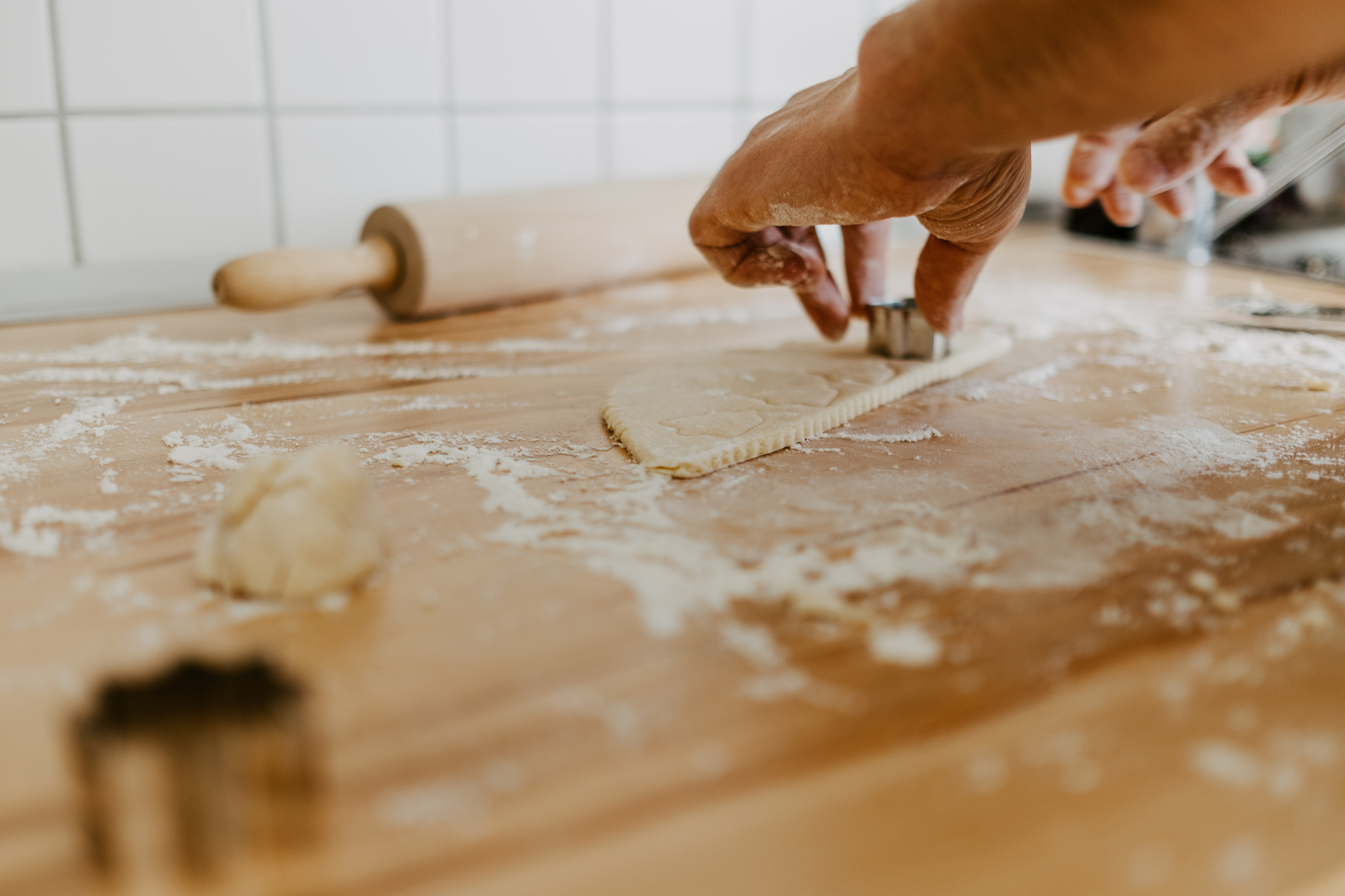 Close-up of hands using cookie cutters on dough, with a rolling pin and more dough on a floured surface in a kitchen
