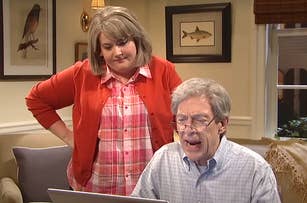 Cecily Strong helps Steve Martin at a computer. They appear to be in a home setting, with framed pictures on the wall behind them