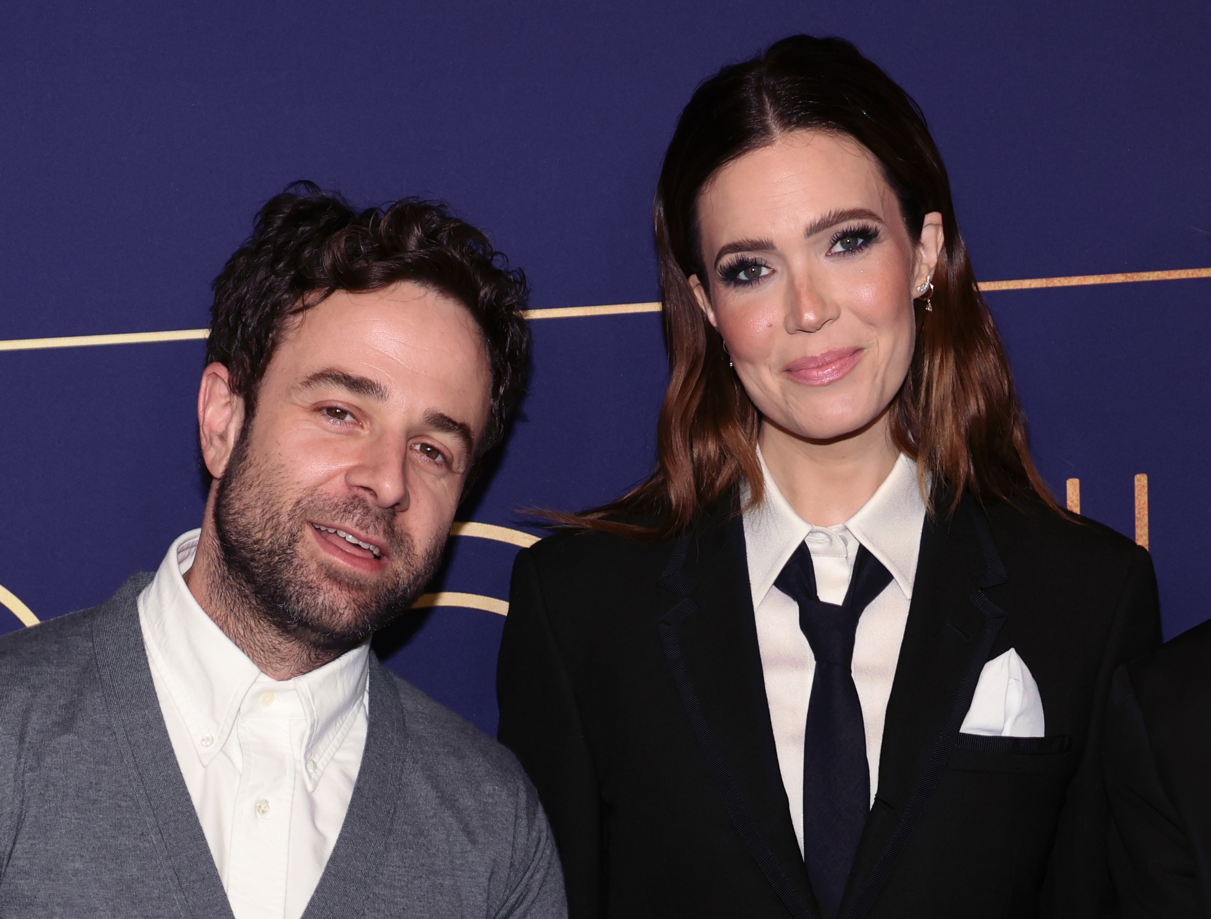 Mandy Moore and Taylor Goldsmith smiling at an event, with Mandy in a suit and tie and Taylor in a blazer over a shirt