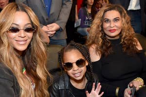 Beyoncé, Blue Ivy Carter, and Tina Knowles sit together at an event, all wearing stylish outfits and sunglasses