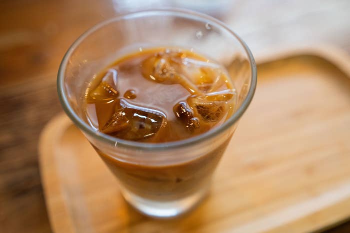 Glass of iced coffee with visible ice cubes on a wooden tray