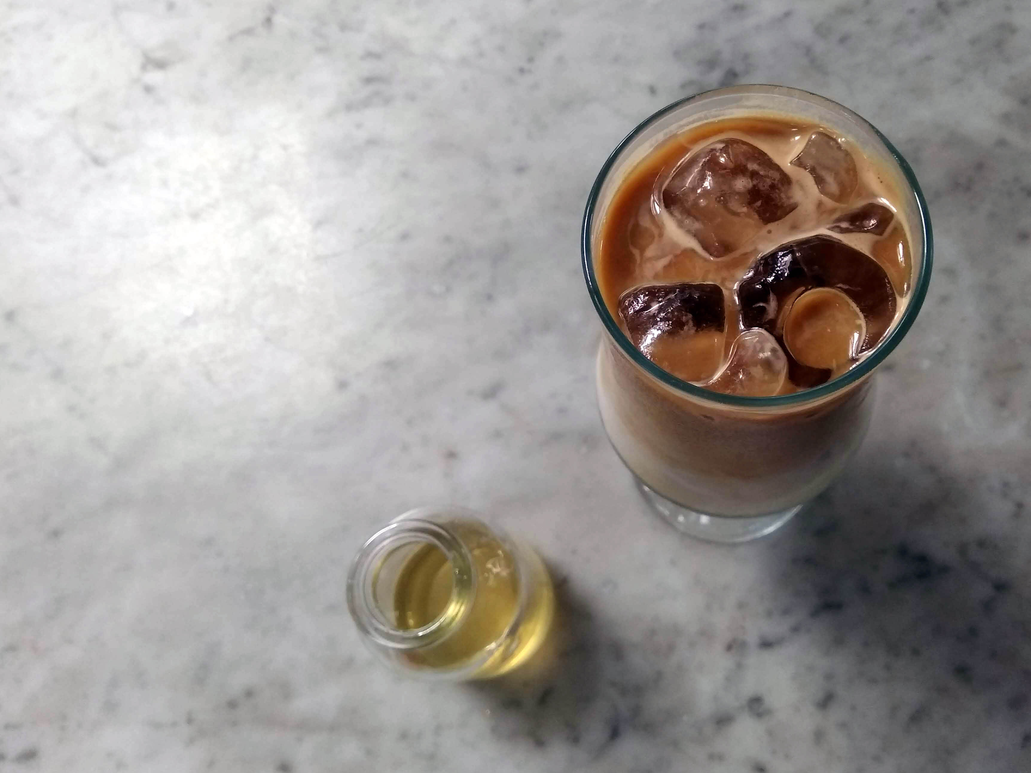 An iced coffee with a bottle of syrup on a marble surface