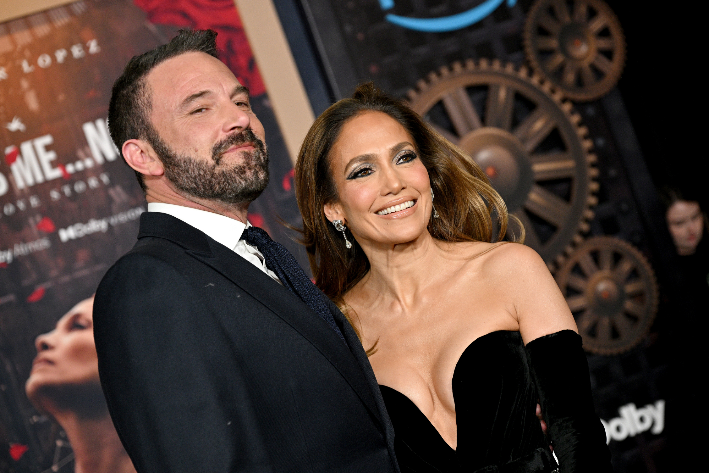 Ben Affleck and Jennifer Lopez posing together on a red carpet; Jennifer in a strapless gown, Ben in a suit and tie