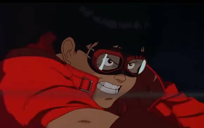 Shot from the film Akira showing the character Kaneda wearing red goggles and a red jacket, looking determined