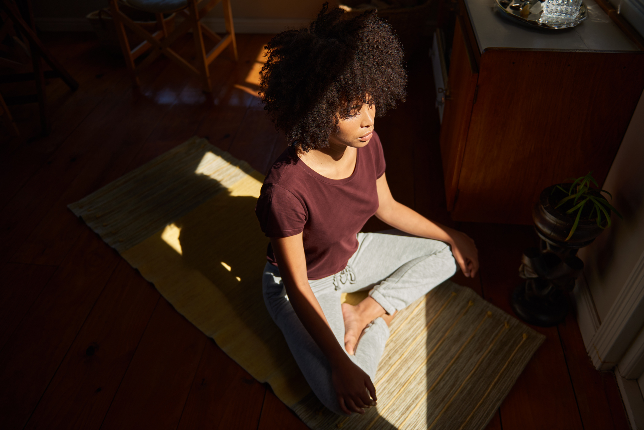En person med krøllete hår sitter med bena i kors på en yogamatte i fredelige omgivelser, og deltar i en meditativ praksis