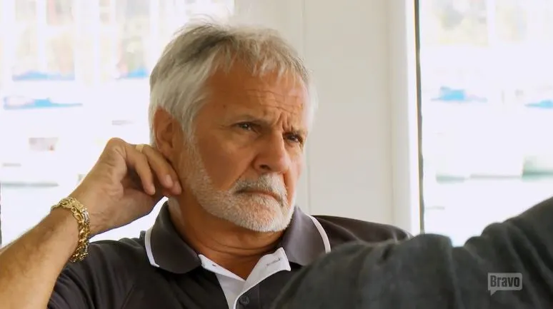 Close-up of Captain Lee Rosbach attentively listening with a thoughtful expression, wearing a casual shirt, taken in a travel-themed setting