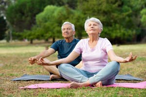 An elderly couple sitting on yoga mats in a park, meditating with closed eyes and relaxed expressions