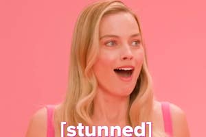 Margot Robbie, with a surprised expression, on a pink background wearing a pink outfit. The word "stunned" appears at the bottom