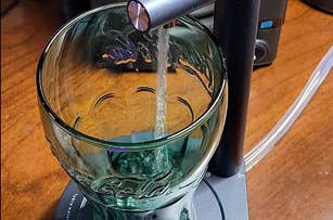 A shot of a glass being filled with water from a desktop water dispenser. The setup is placed on a wooden surface