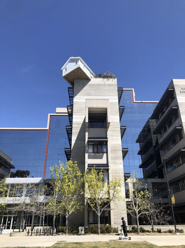 An innovative building with a small upside-down house on its rooftop. A person rides a scooter in front