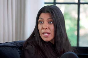 Kourtney Kardashian in a casual conversation, wearing a dark sweatshirt, indoors with a window in the background. The scene is from an "E!" network feature