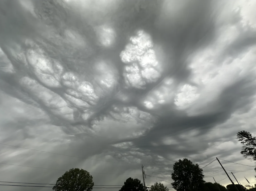 Stormy sky with dramatic, swirling clouds forming intricate patterns above silhouetted tree tops and power lines