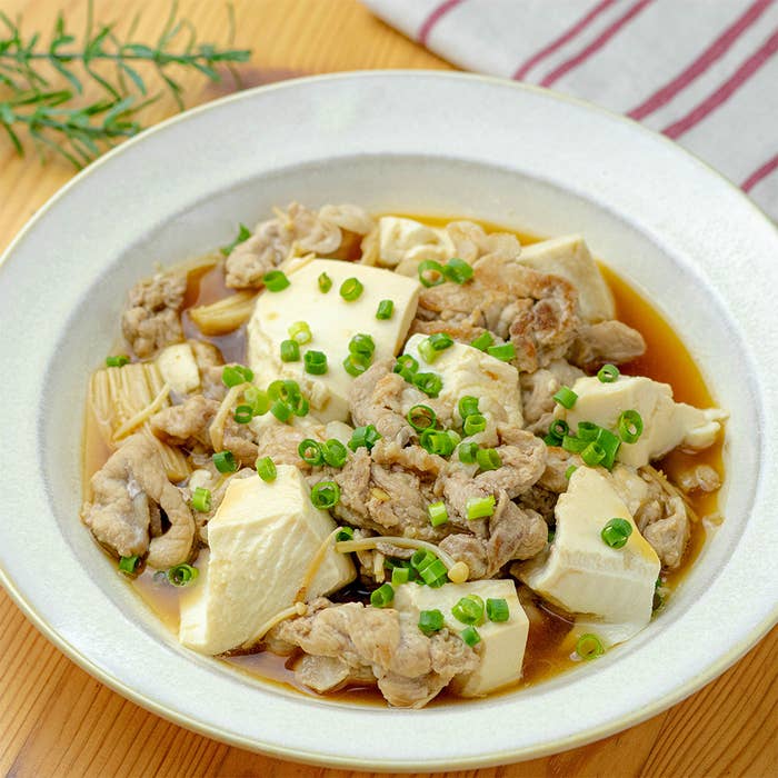 豆腐と薄切り肉のたっぷりのネギが乗った美味しそうな煮物。白い皿に盛られ、シンプルながらも家庭的な一品。