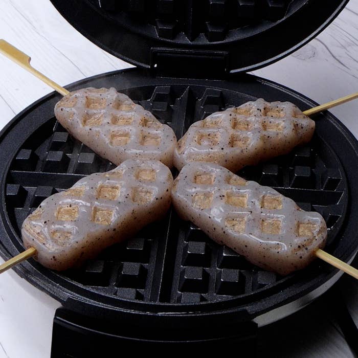 ワッフルメーカーで焼かれている串に刺さったこんにゃく。