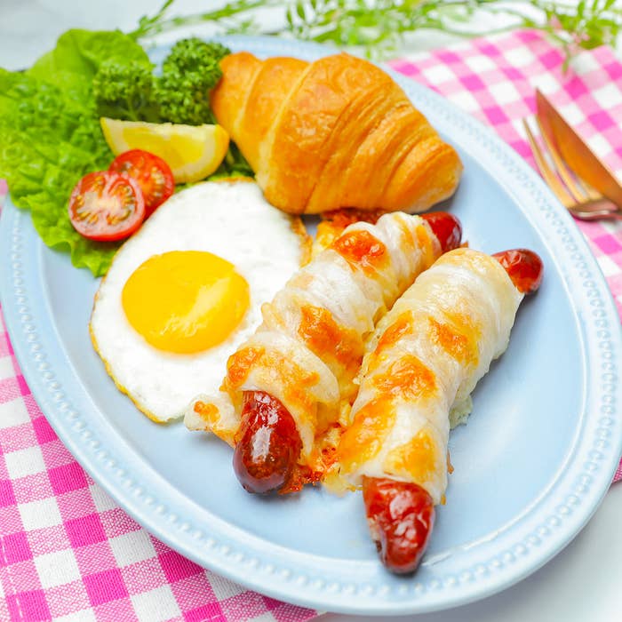 クロワッサン、目玉焼き、野菜、ソーセージのチーズ焼きが乗った青い皿。