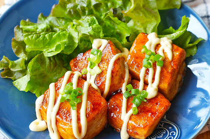 青い皿に盛り付けられた、レタスとマヨネーズとネギをトッピングした照り焼き豆腐の料理。