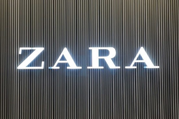 A metal wall with vertical lines and the illuminated text “ZARA” in the center