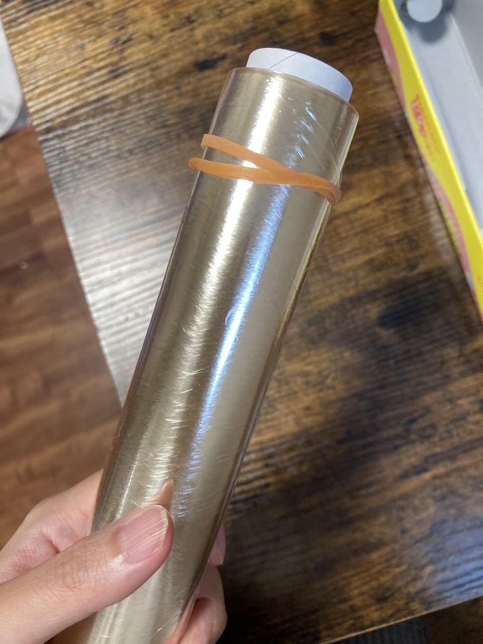 人が手に持っているプラスチック製のラップのロール。ゴムバンドがロールに巻かれている。