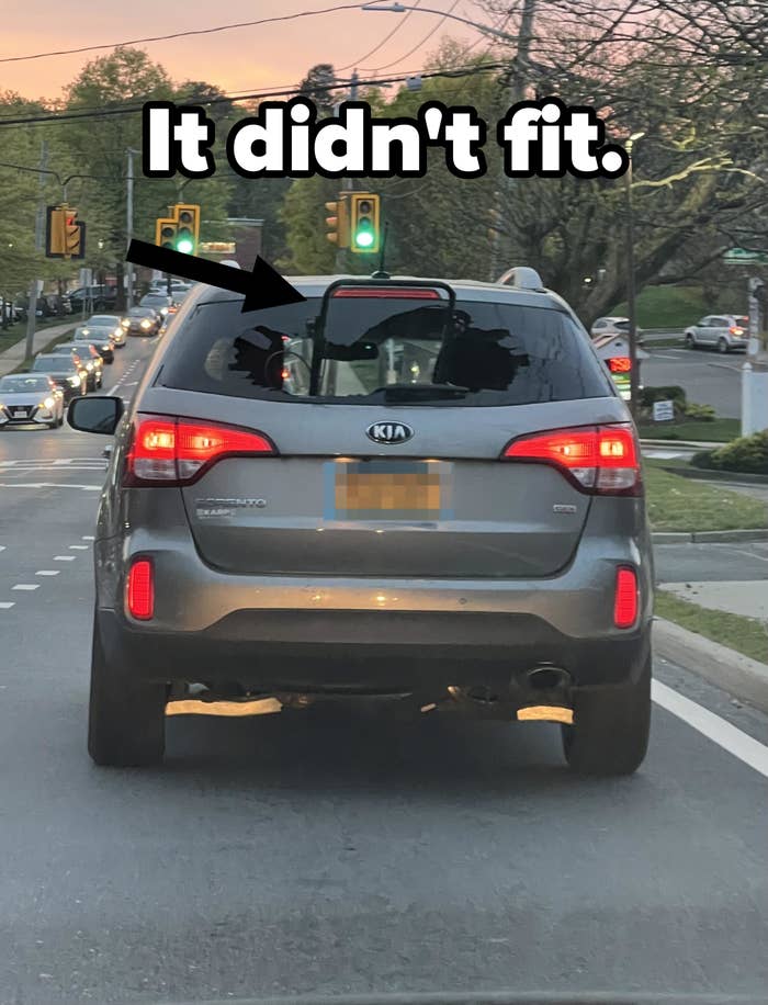 Rear view of a Kia vehicle on the road with brake lights on, other vehicles and traffic lights in the background