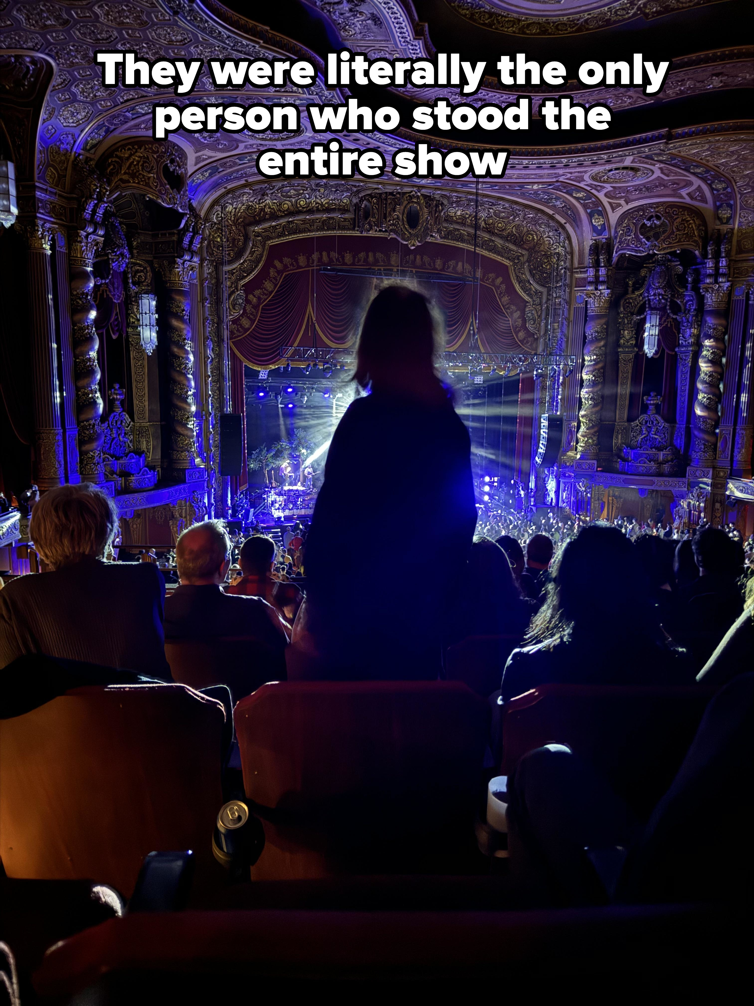 Audience view from balcony seats at a live theater performance, with focus on stage and silhouettes of attendees