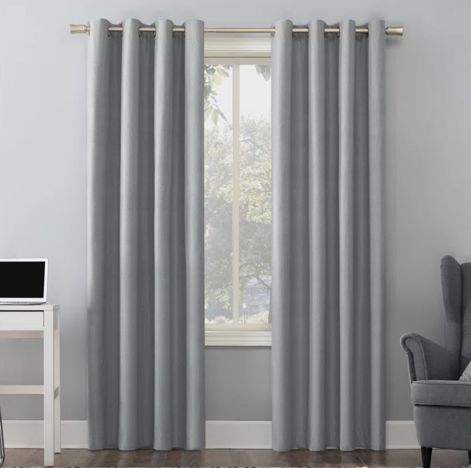 A pair of gray blackout curtains in a room, window partially visible, with an armchair and desk to the sides