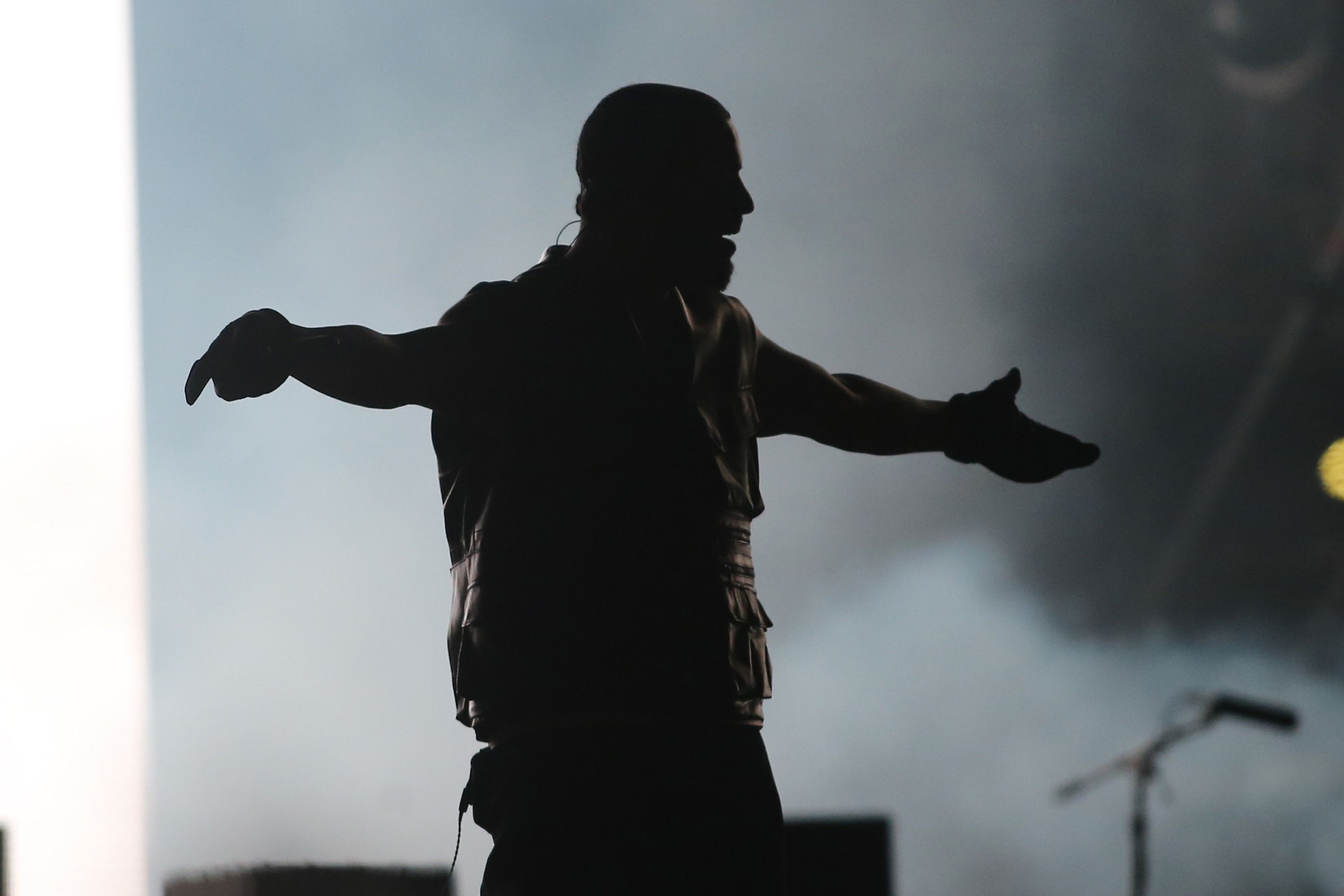 Silhouetted performer with arms extended on a concert stage, engaging with the audience