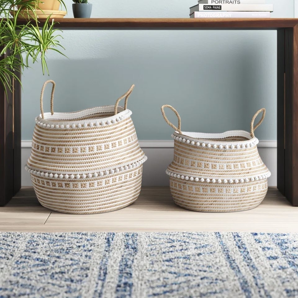 Two woven baskets with handles on a floor beside a shelf, featuring neutral tones and patterns