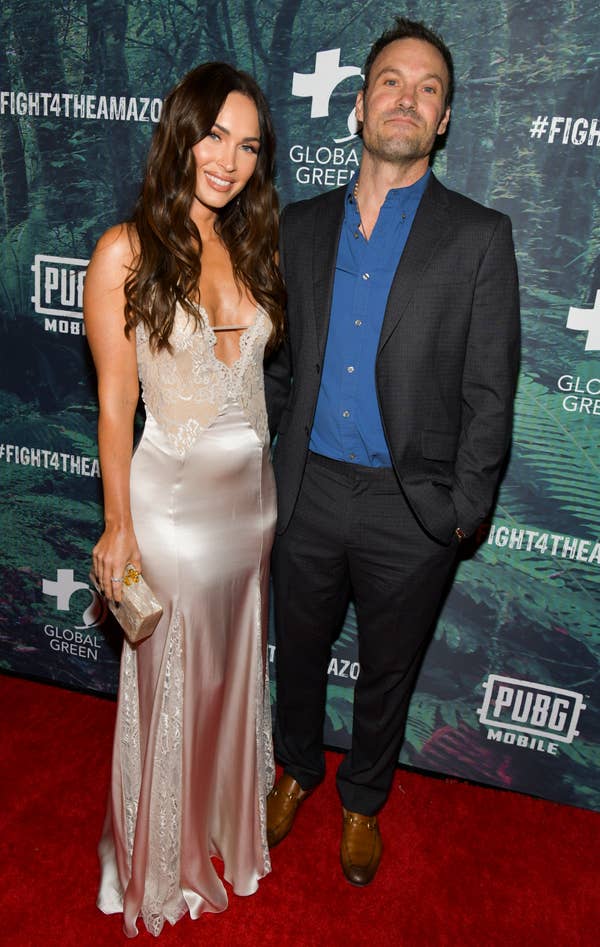 A couple on the red carpet; woman in a satin gown, man in a suit with unbuttoned blue shirt