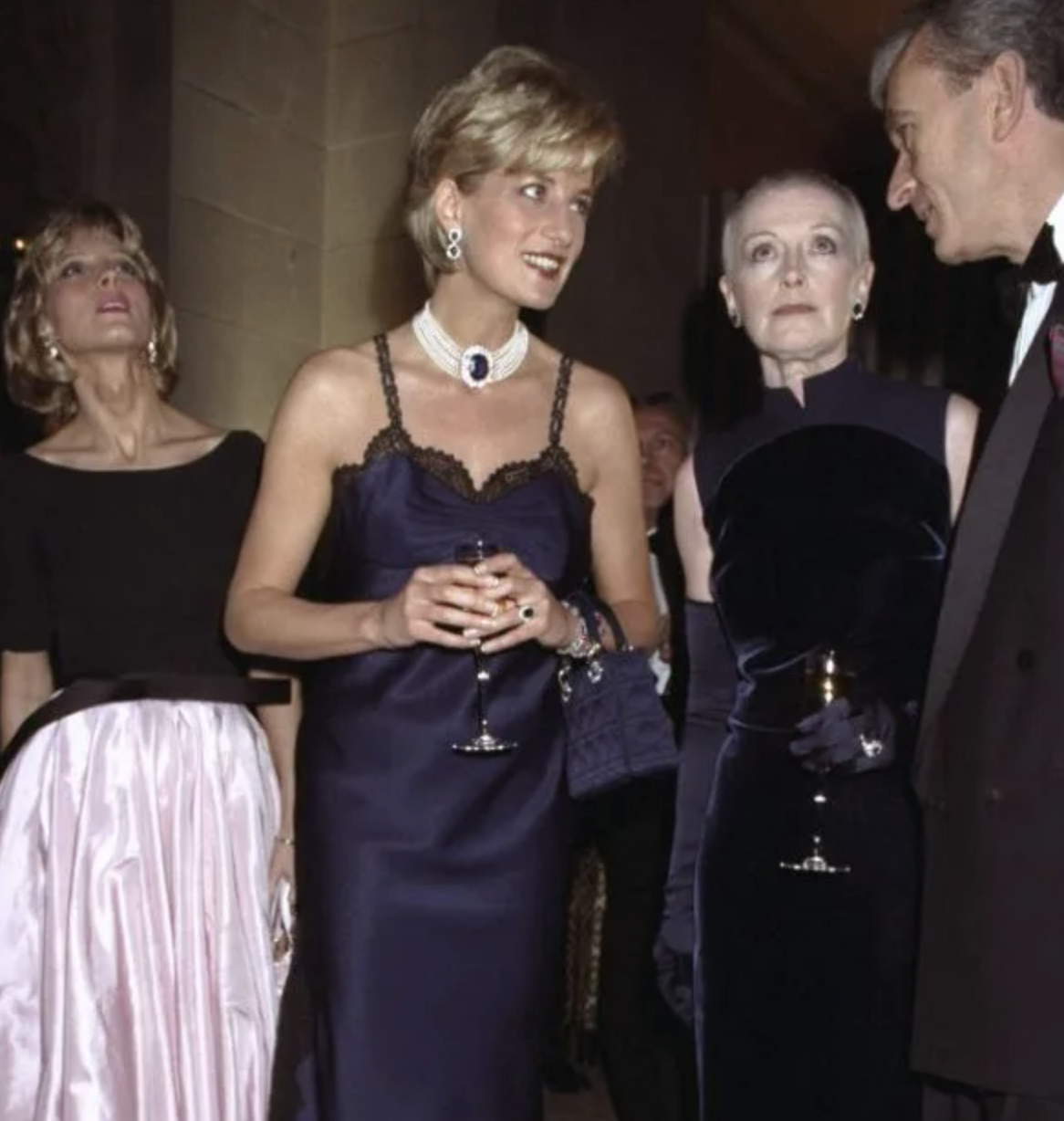 Princesa Diana en vestido de gala azul, conversando con invitados en un evento formal